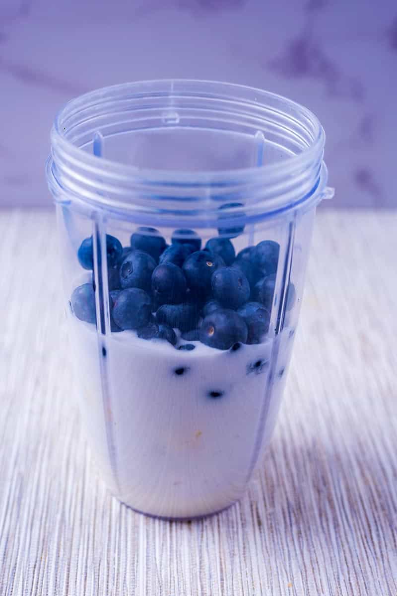 A blender jug containing milk and blueberries.