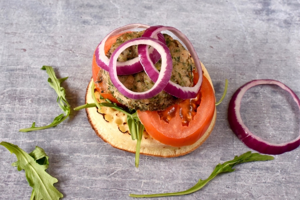 A Crumpet topped with a burger, tomato and onion rings