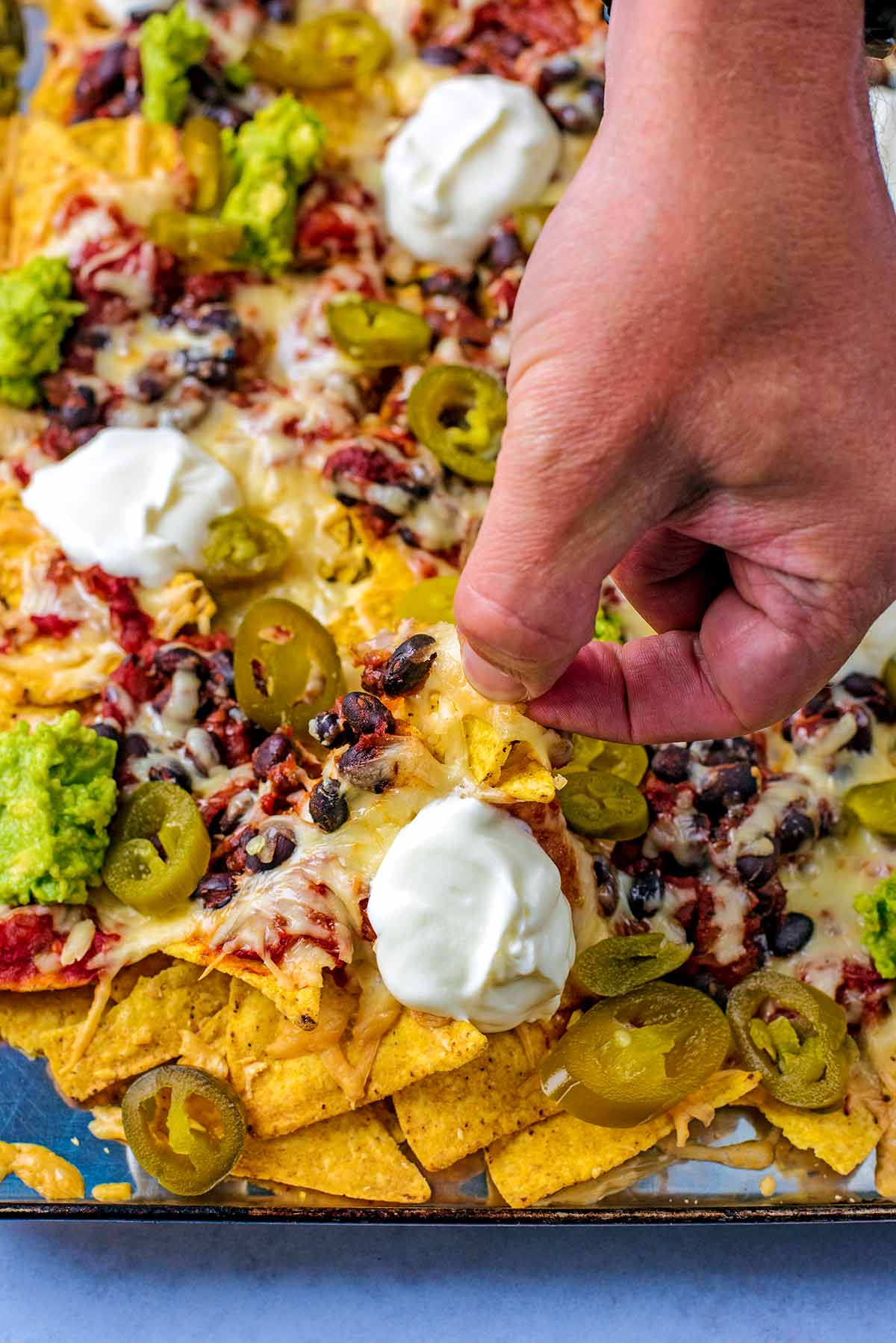 A hand picking up a cheese and bean covered nacho from a tray.