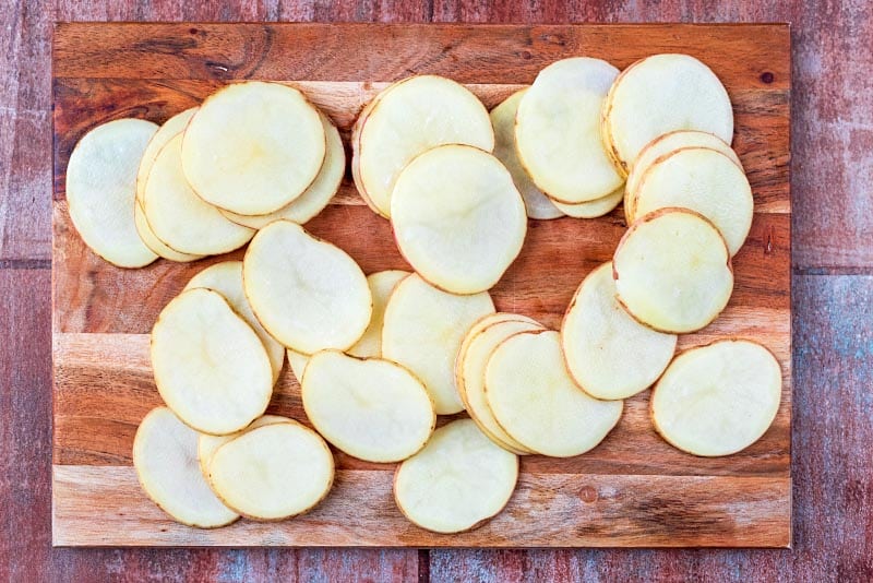 A wooden chopping board with very thinly sliced potatoes.