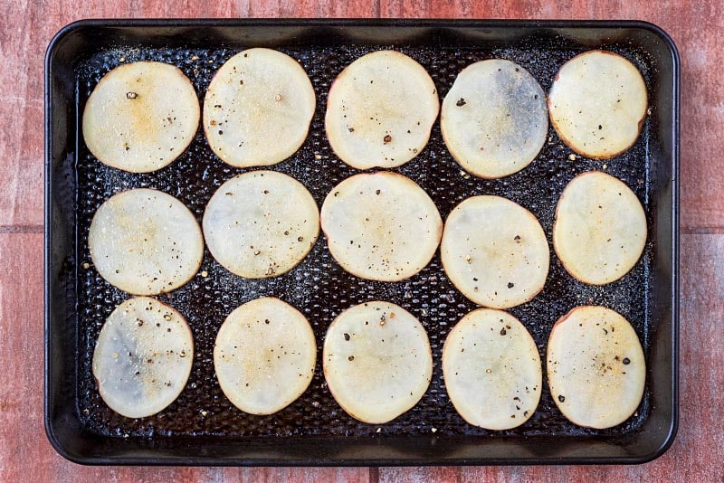 A baking tray with a layer of thinly sliced potatoes.