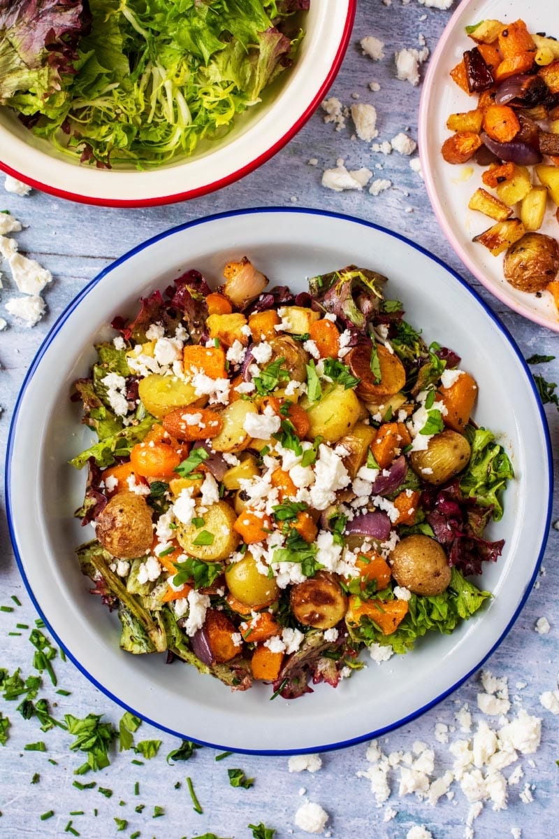 Roasted Vegetable Winter Salad in a white bowl next to salad leaves and a plate of vegetables