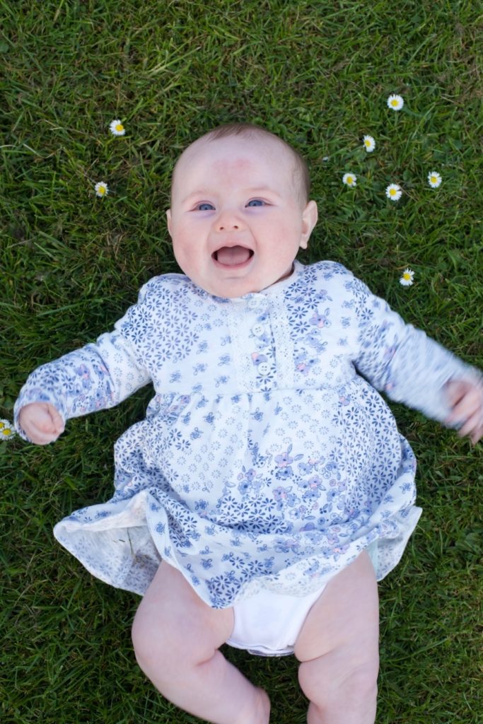 A laughing baby laying on the grass.