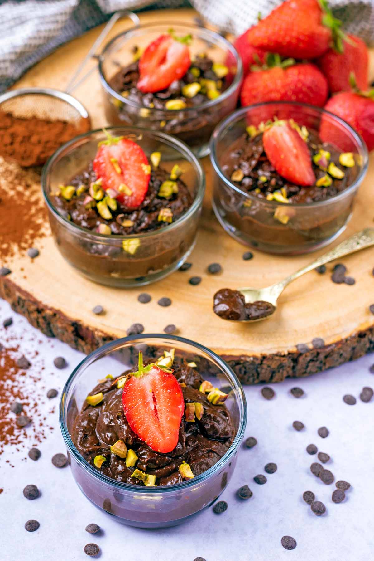 Serving glasses of chocolate pudding next to a pile of strawberries.