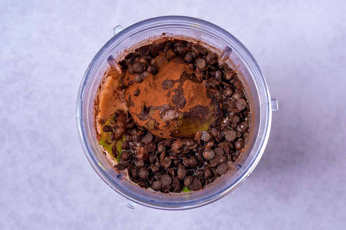 A blender jug containing avocado, cocoa, chocolate chips and maple syrup.