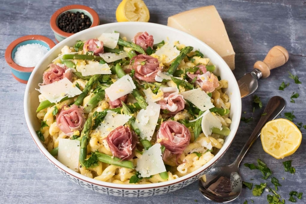 Cooked pasta spirals topped with asparagus, ham and shaving of cheese.