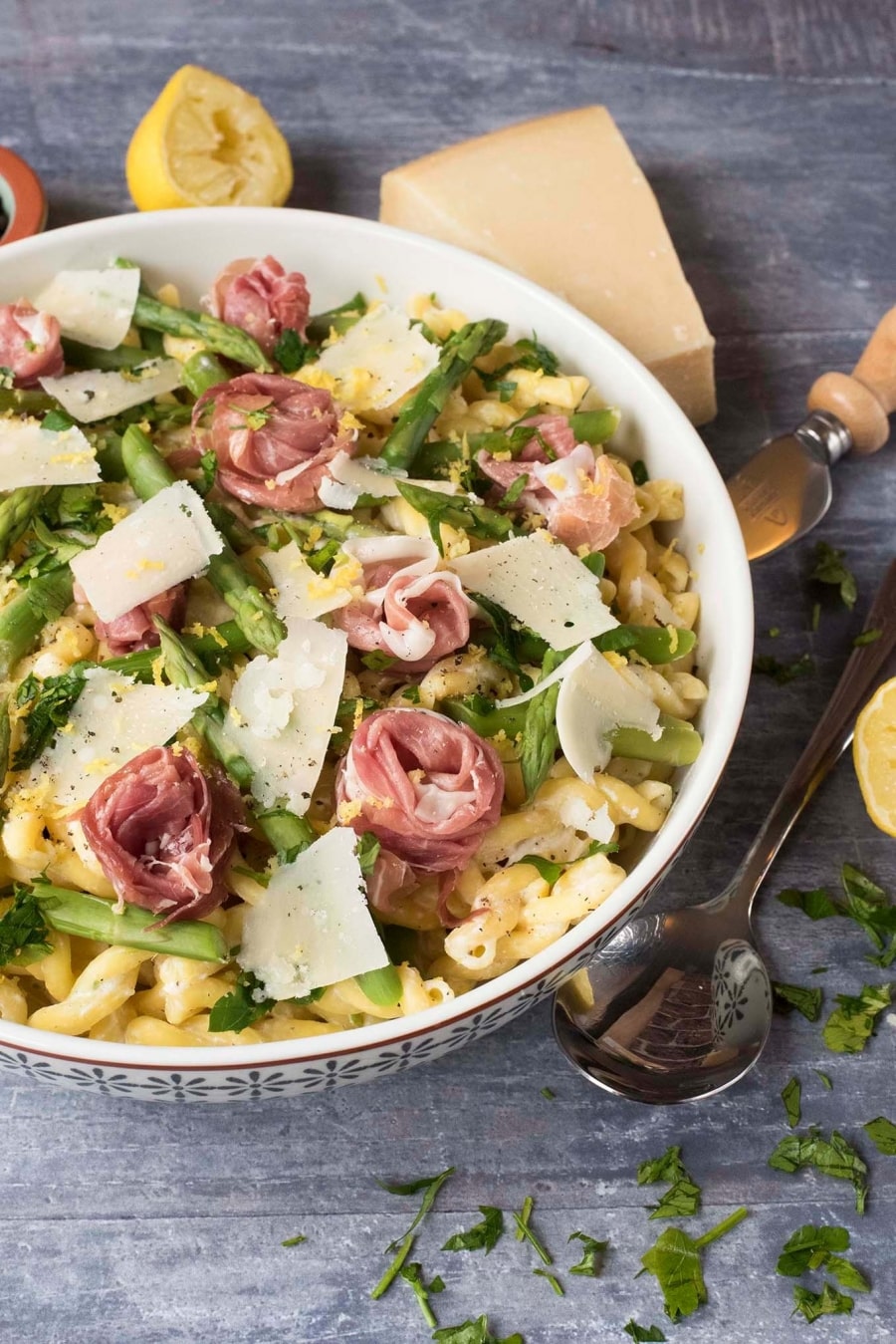 Prosciutto curled into rose shapes on top of a bowl of pasta and asparagus.