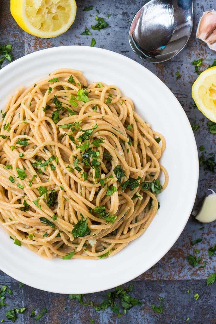 A white dish with a large pile of spaghetti topped with chopped herbs.