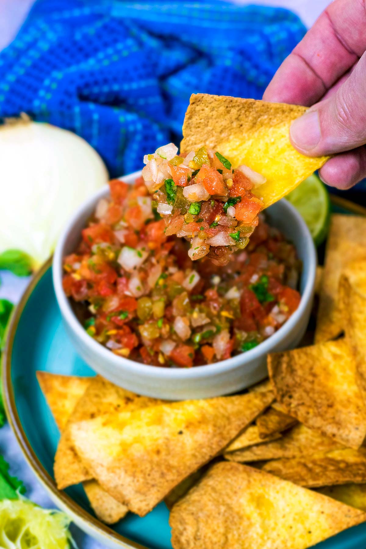 A hand scooping salsa with a tortilla chip.