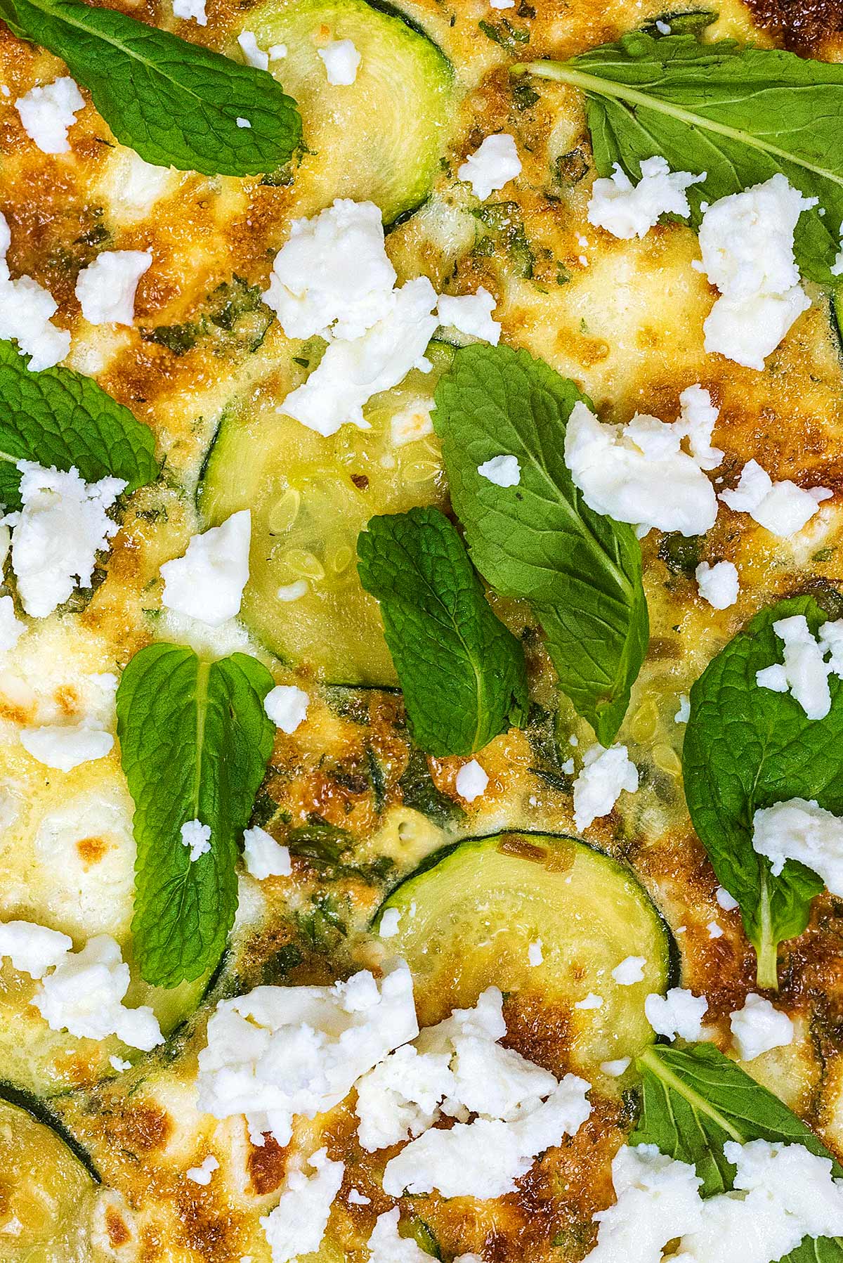 Slices of courgette in a frittata topped with mint leaves and crumbled feta.