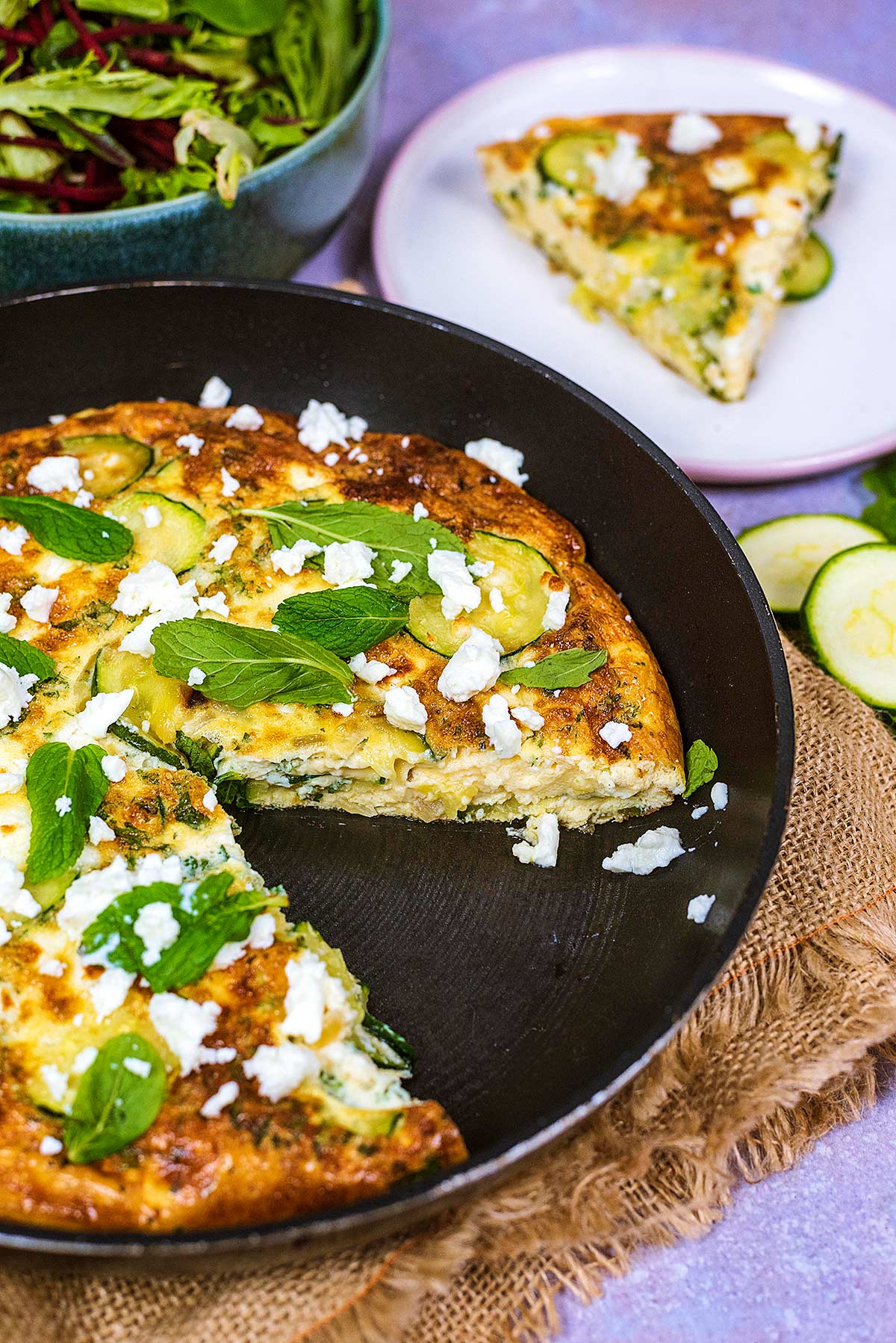 A pan of cooked frittata with a slice removed and put on a plate in the background.