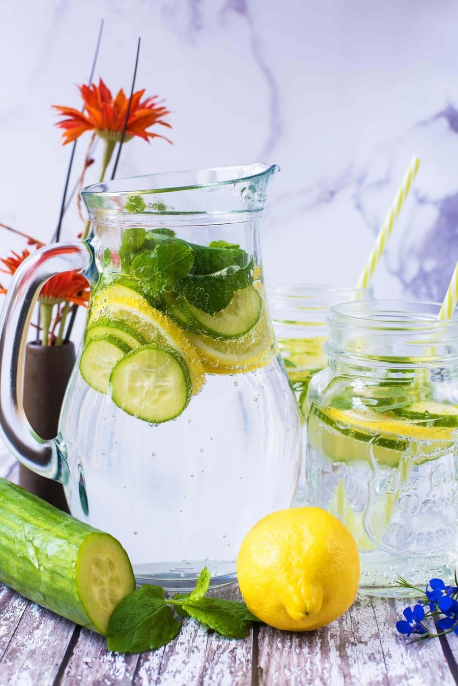 A large glass jug of water with slices of cucumber and lemon in it.