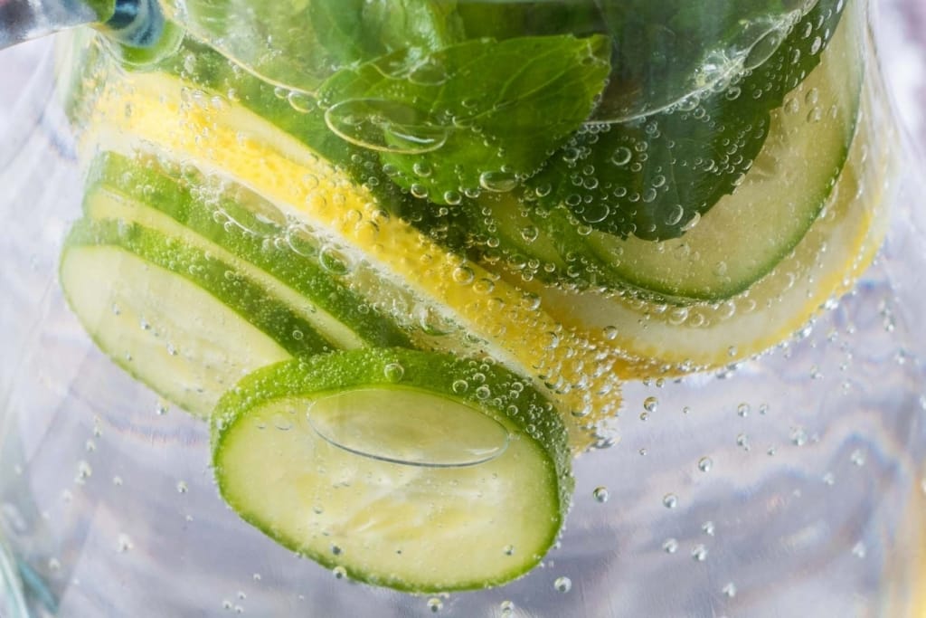 Slices of cucumber and lemon and mint leaves in sparkling water.