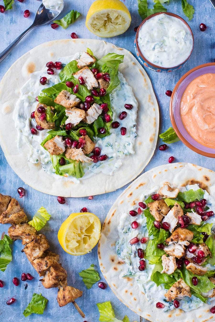 Two flatbreads covered in a white sauce, lettuce, chicken chunks and pomegranate seeds.
