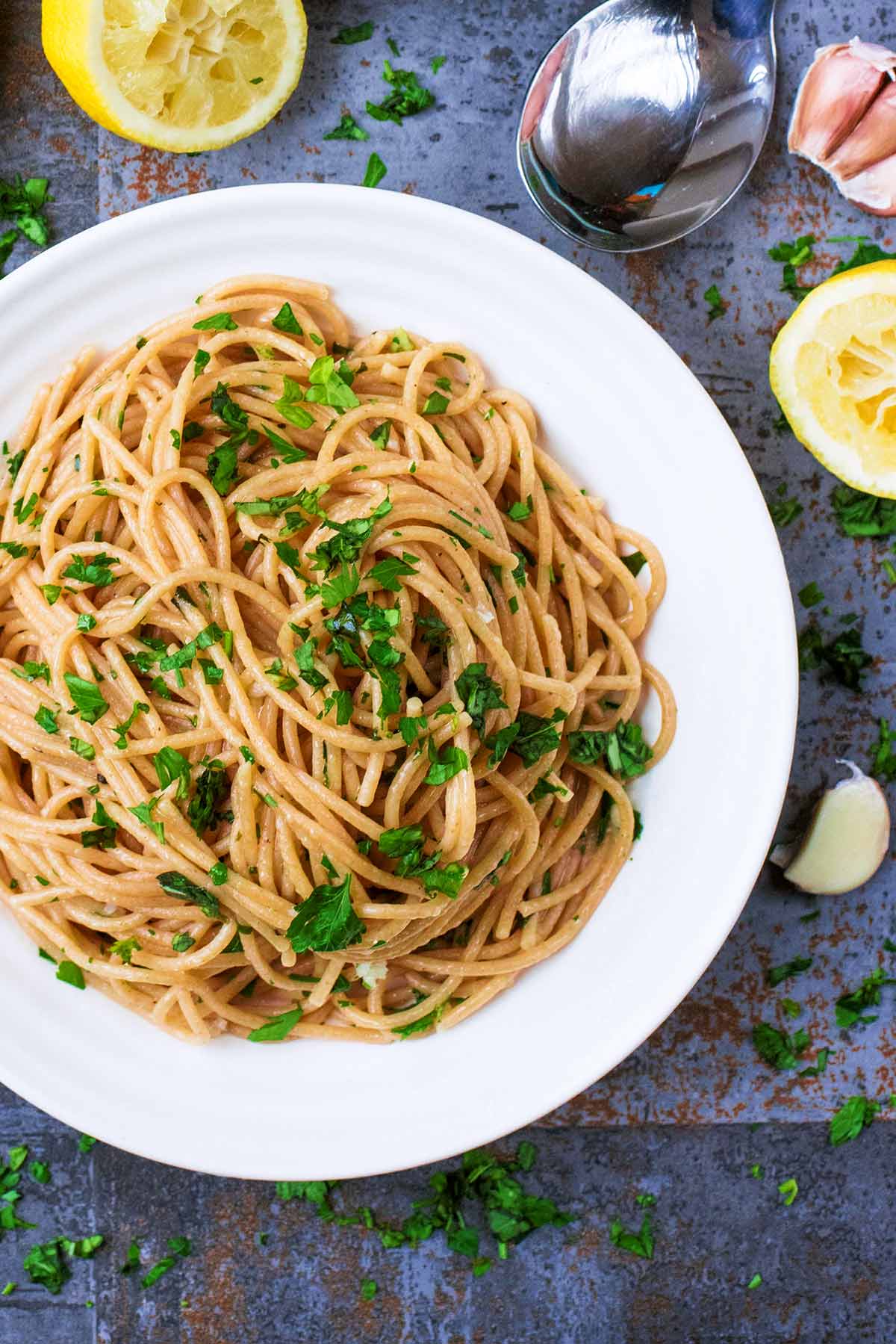 A white dish with a large pile of spaghetti topped with chopped herbs.