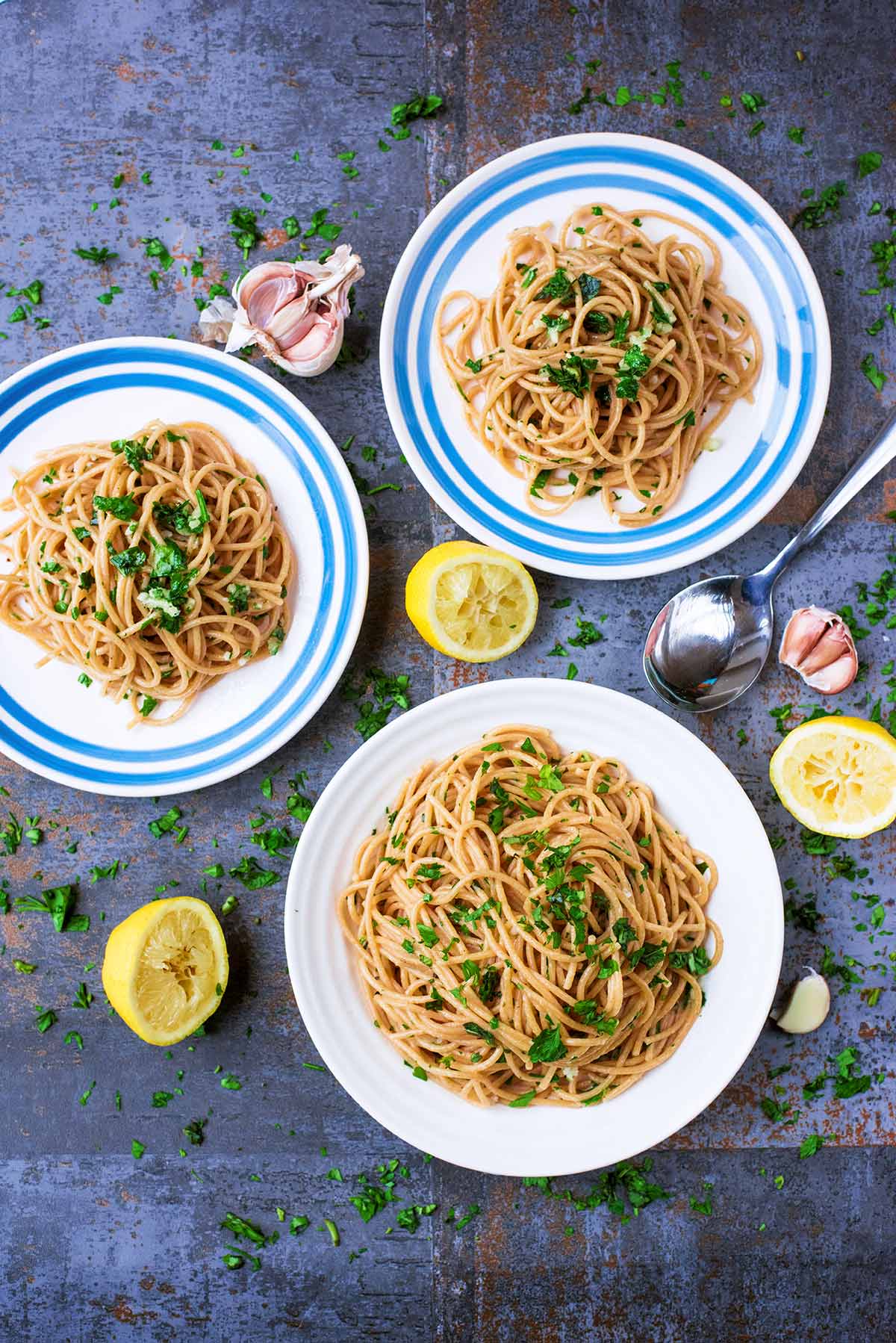 Three plates of herbs mixed into cooked spaghetti.