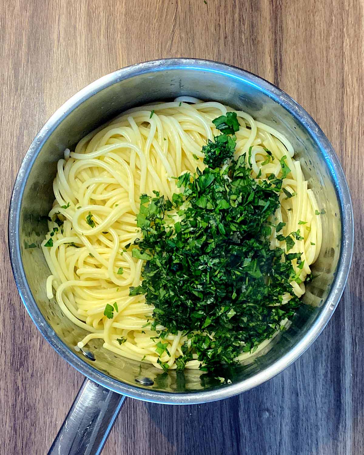 Chopped herbs and oil added to the pan of spaghetti.