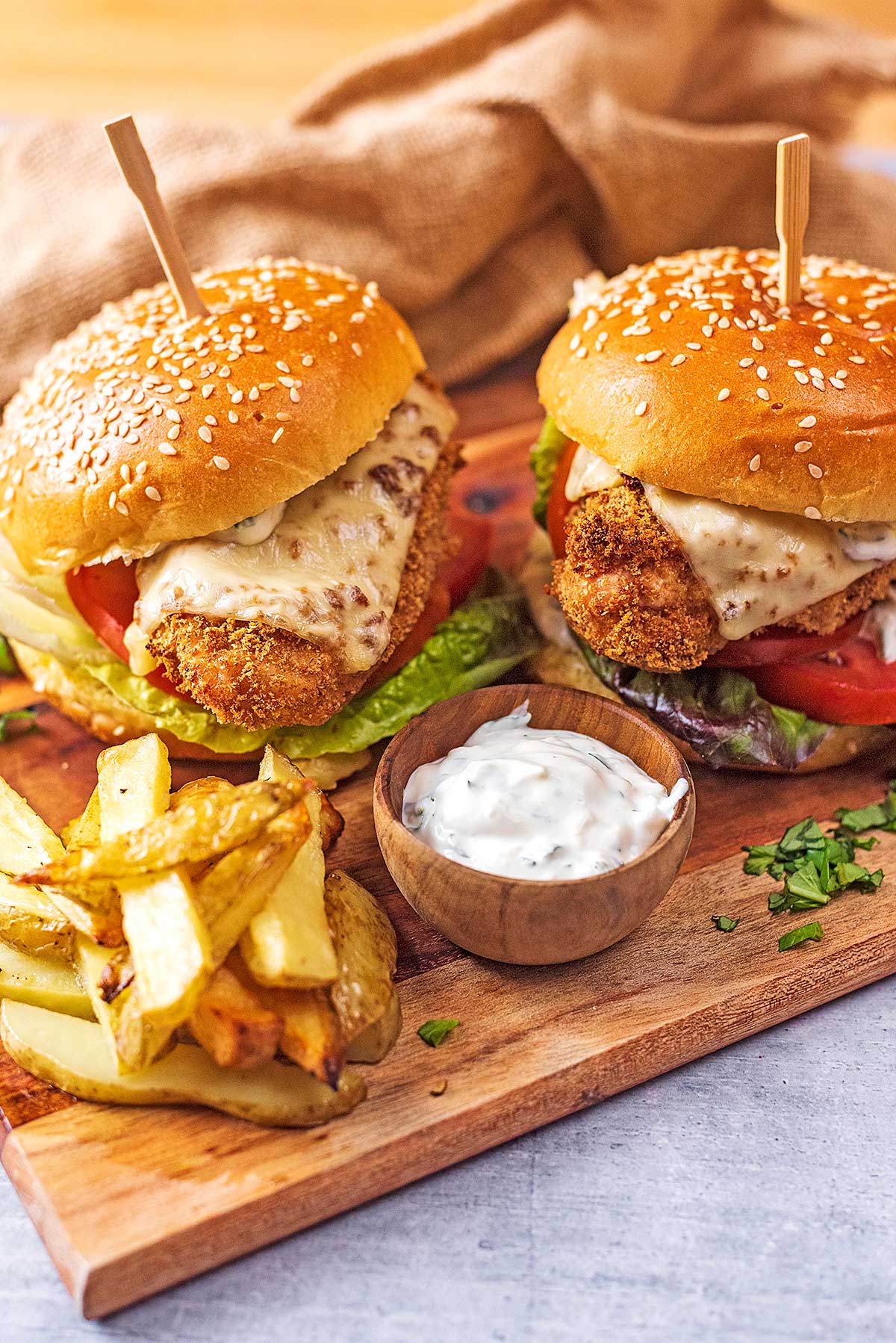Two chicken burgers with fries and dip on a wooden serving board