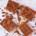 Four Chocolate Peanut Butter Oat Squares surrounded by crumbs on a wooden surface.