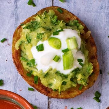 Loaded potato skin topped with cream and spring onions on a wooden surface.