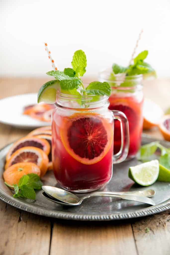 A deep red coloured drink in a mason jar with mint leaves sticking out