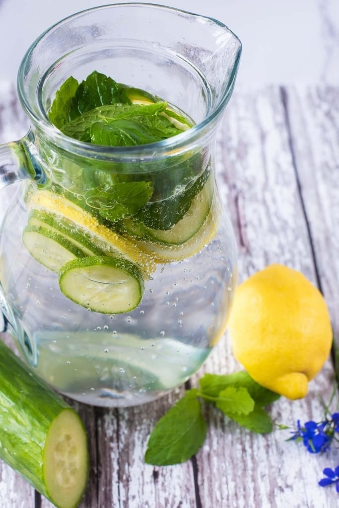 A glass jug containing slices of cucumber and lemon and some mint leaves