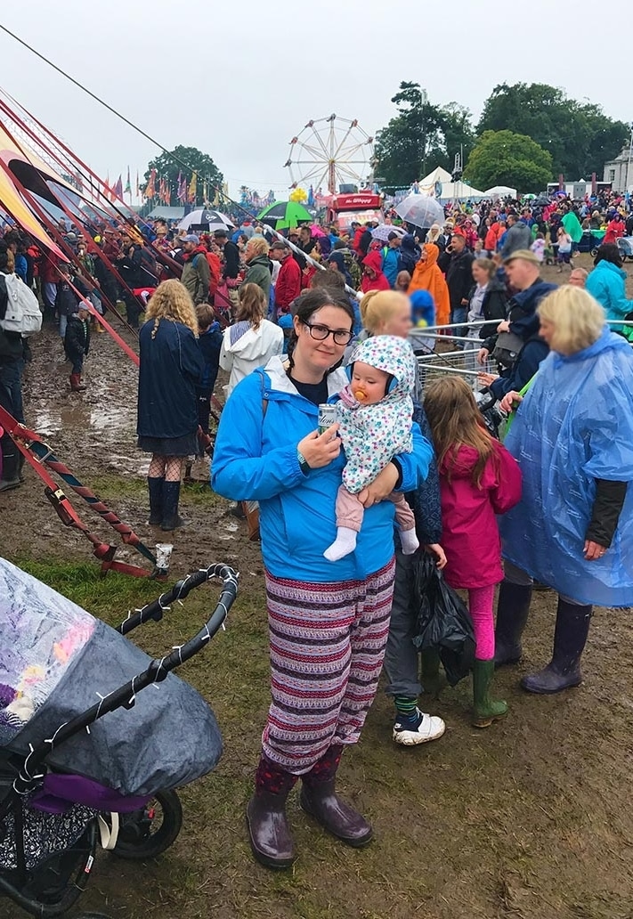 A woman holding a baby at a muddy festival.