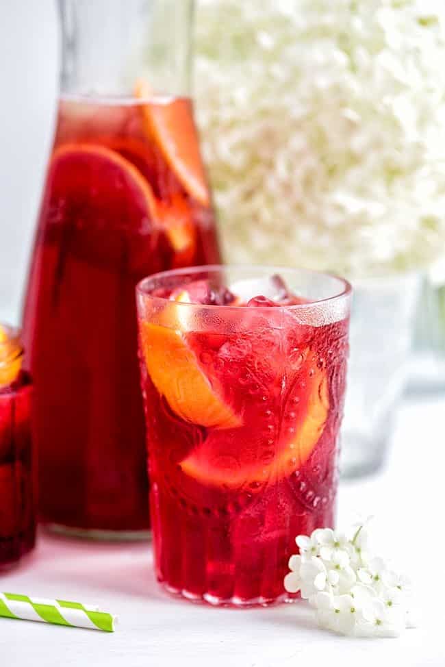 A bright red drink in a glass with wedges of oranges