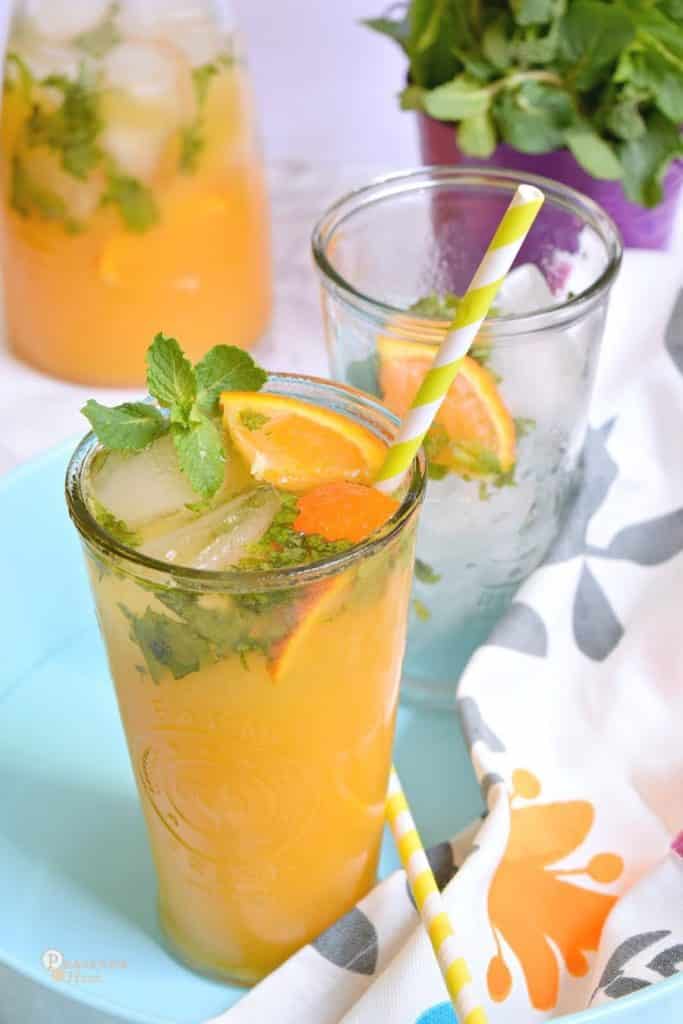 An orange drink in a tall glass with orange slices and mint leaves