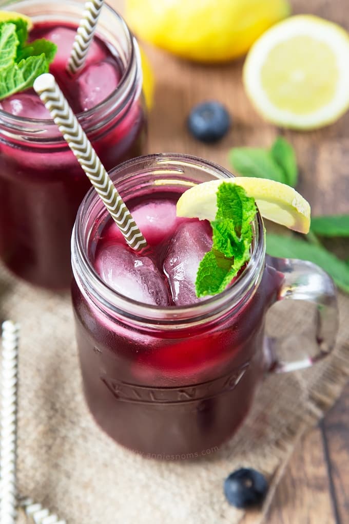 A mason jar containing a purple drink with mint leaves and a slice of lemon