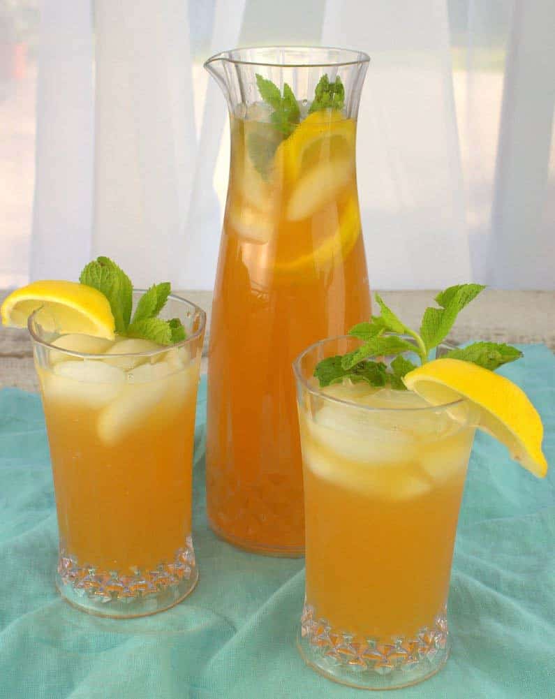 Two glasses of yellow iced tea in front of a jug of more iced tea