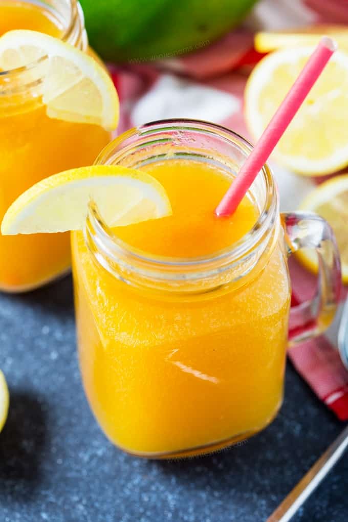 A bright yellow drink in a mason jar with a lemon slice and pink straw