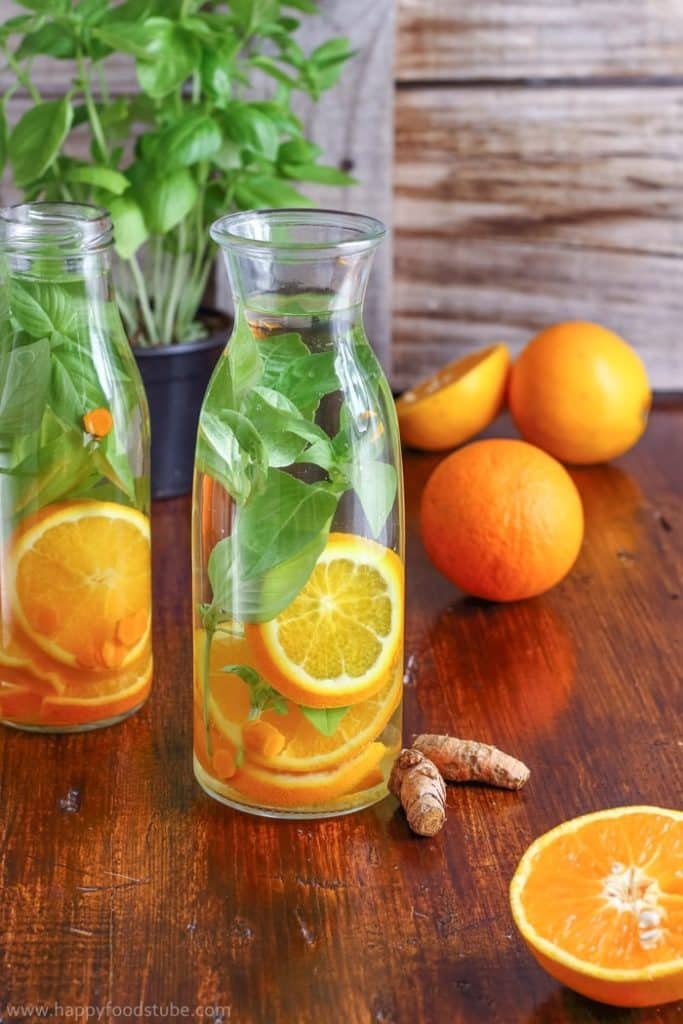 A tall jug or water with orange slices and basil leaves in it