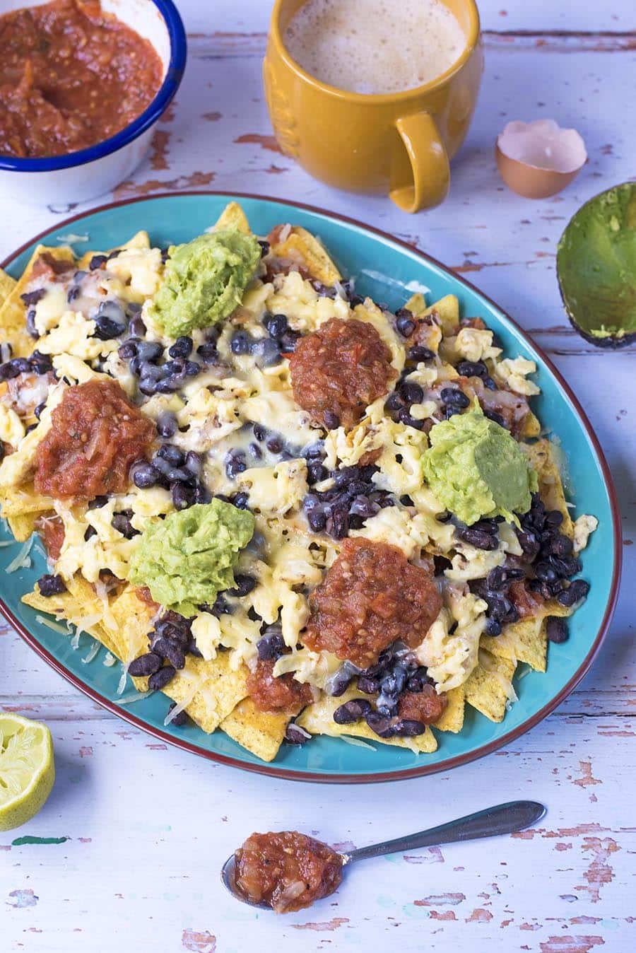 A plate of nachos with a cup of coffee and pot of salsa.