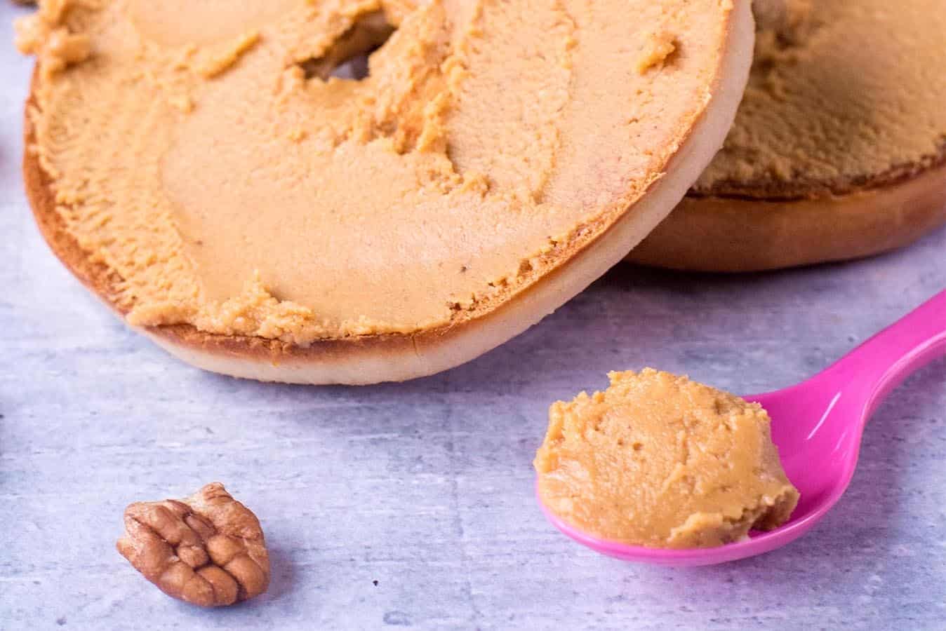 Pecan Butter spread on a bakel and some on a pink spoon.