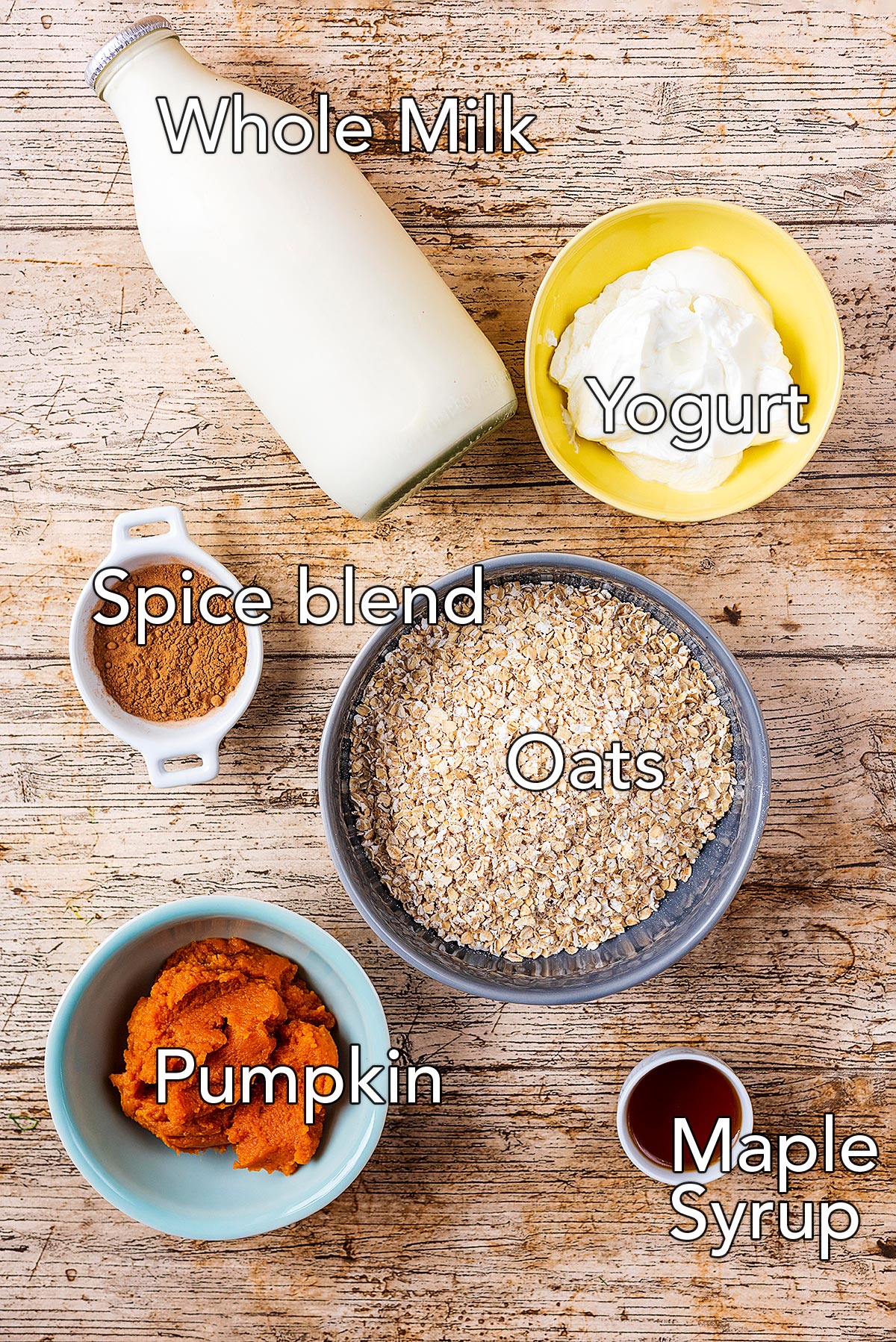 A bottle of milk with bowls of yogurt, oats, spices, pumpkin and maple syrup.