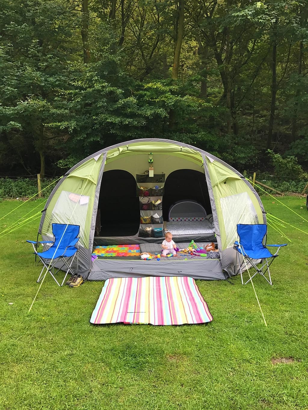 A baby sat in a green tent with two blue chairs.