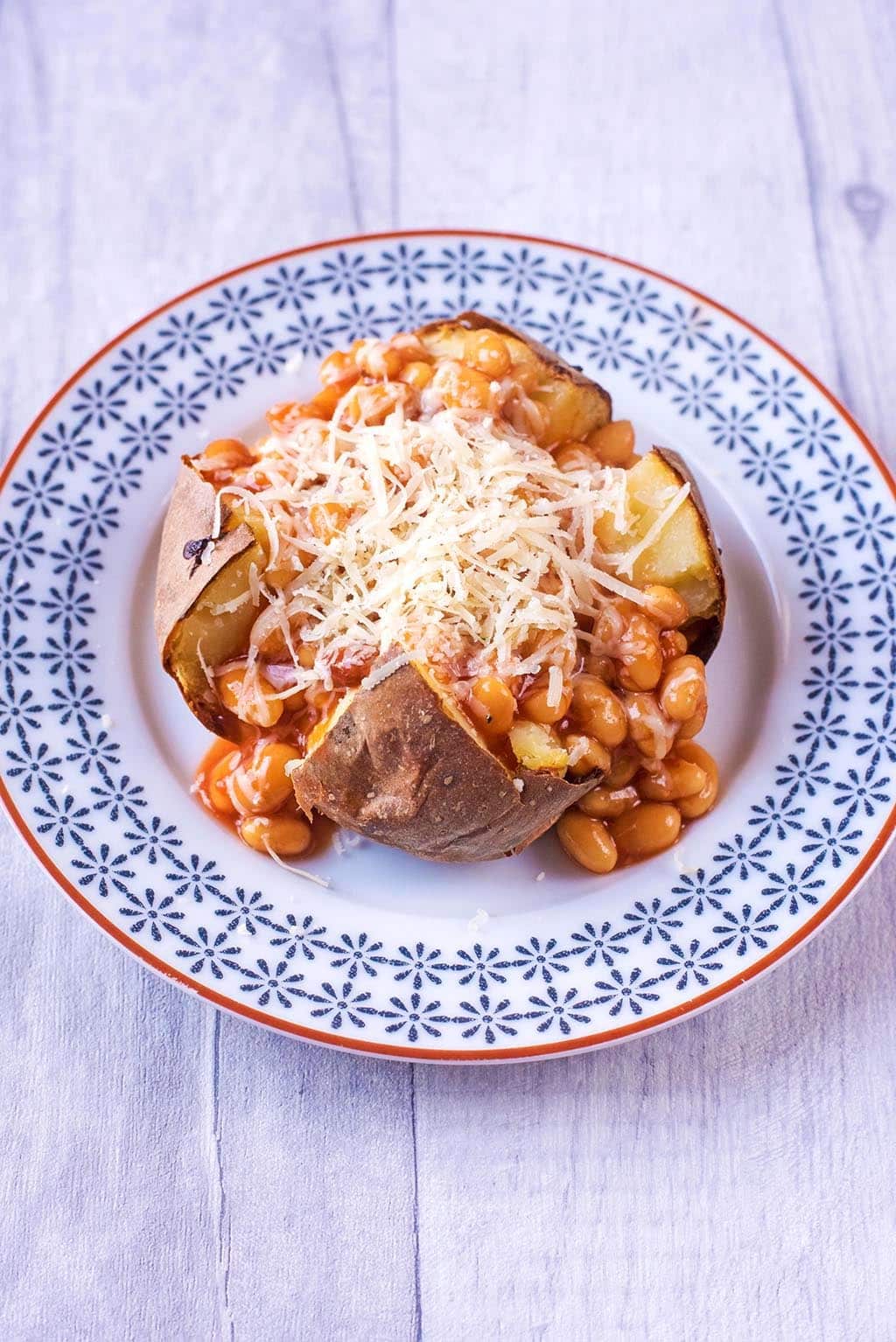 Baked Potato topped with Baked Beans and Cheddar on a patterned plate.