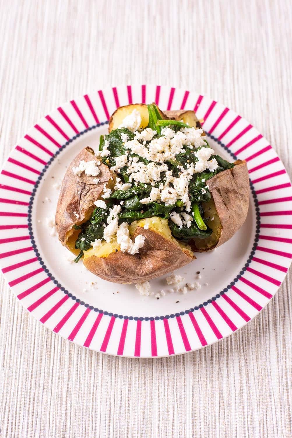 Baked Potato topped with Spinach and Feta on a red and white plate.