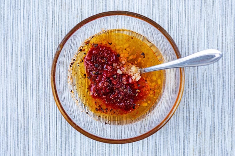 A glass bowl containing harissa paste, oil, honey and garlic.