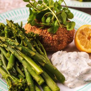 Tuna Fish cakes on a plate with vegetables, tzatziki and a lemon wedge