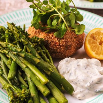 Tuna Fish cakes on a plate with vegetables, tzatziki and a lemon wedge