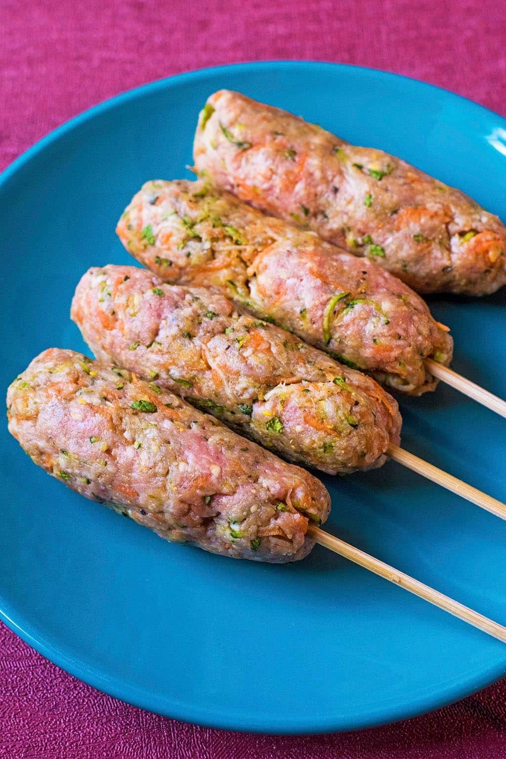 Four uncooked lamb koftas on a blue plate.