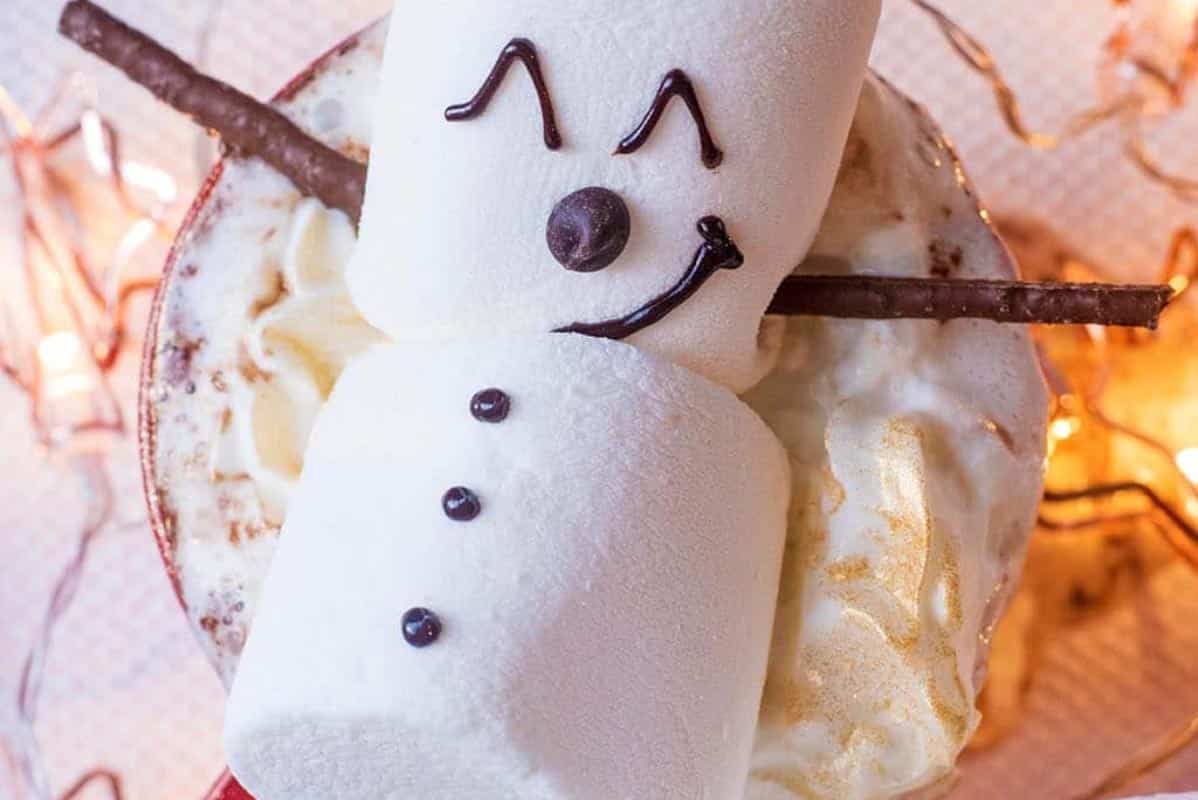 A marshmallow snowman on top of cream topped hot chocolate.