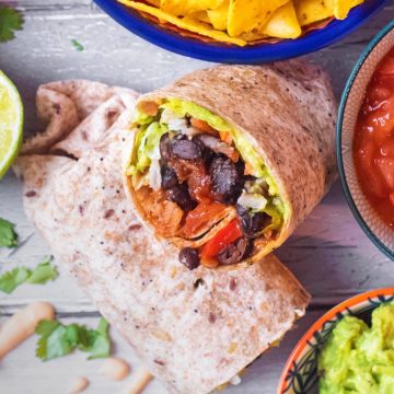 Bean Burrito surrounded by salsa, chips, guacamole and coriander leaves