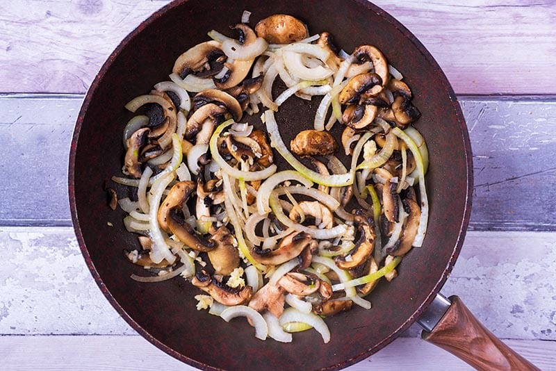 Sliced mushrooms, onions and garlic frying in a pan.