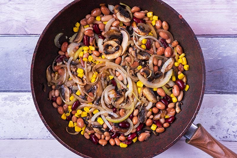 Mushrooms, onions, beans and sweetcorn frying in a pan.