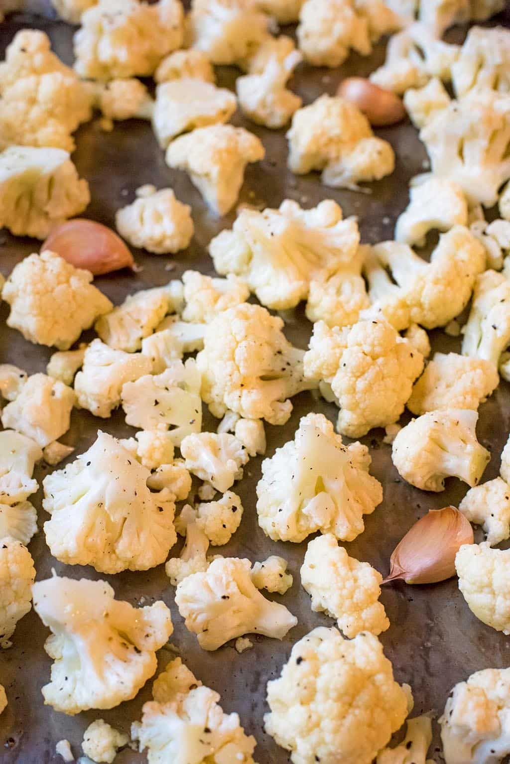 A tray of cauliflower florets and garlic cloves, seasoned with pepper.