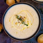Creamy Roasted Cauliflower Soup in a bowl drizzled with cream and oil, topped with herbs.