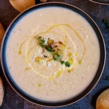 Creamy Roasted Cauliflower Soup in a bowl drizzled with cream and oil, topped with herbs.